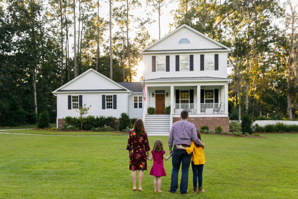 Family of Four With Daughters Looking at Their New Construction White Farmhouse Home